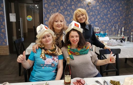 Группа женщин празднует за накрытым столом в бумажных коронах